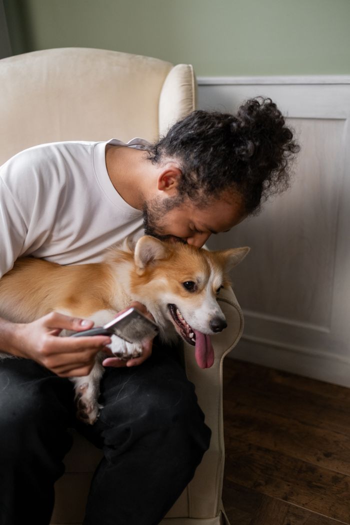 The Art of Drawing Readers In: Your attractive post title goes here A man sitting indoors, lovingly embracing his pet corgi on a comfortable chair.